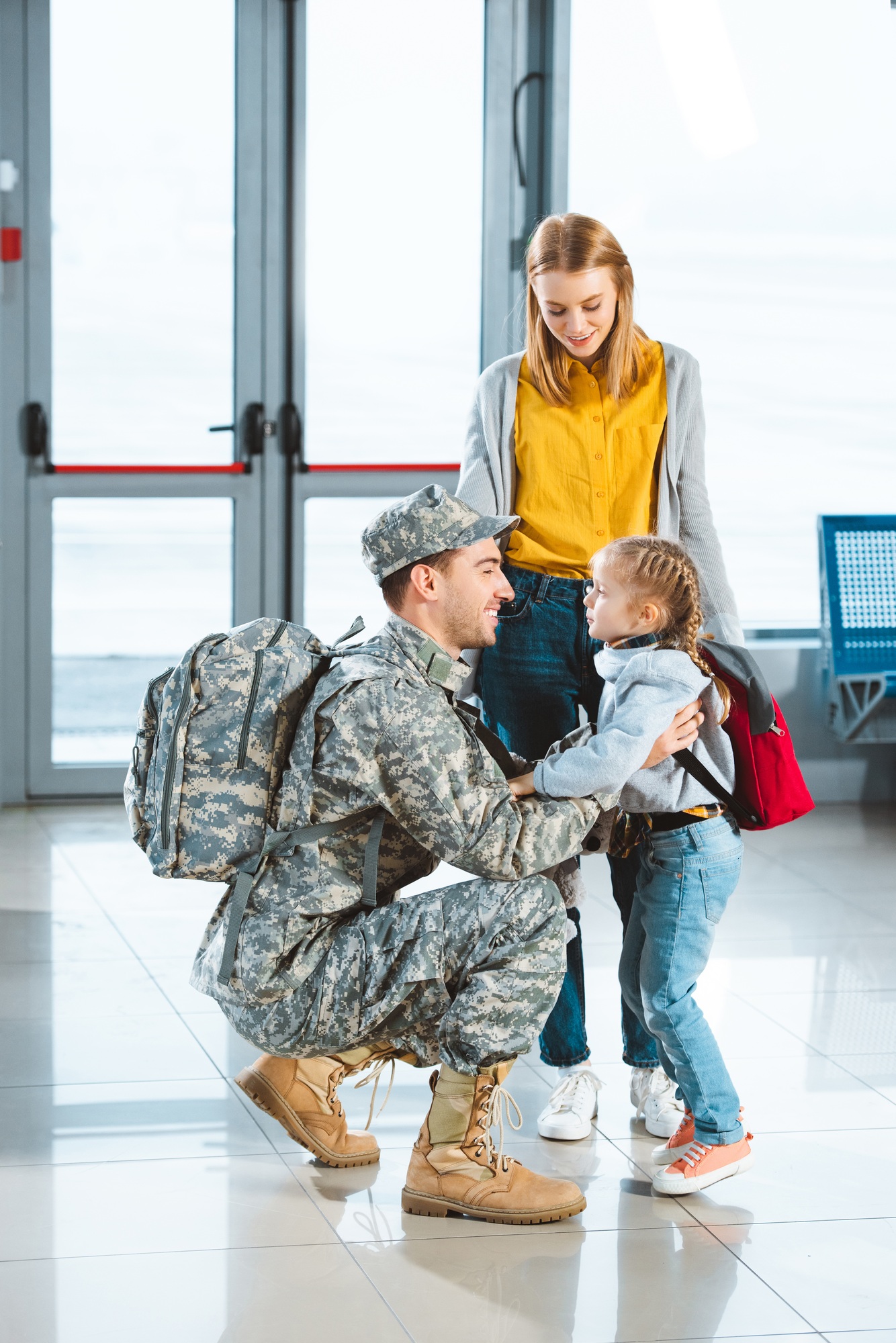 cheerful dad in military uniform hugging daughter near wife in airport